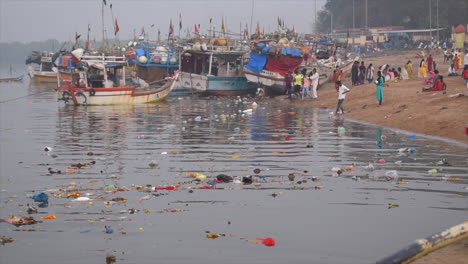 Closeup-of-Water-pollution-near-a-sea-shore,flowers,-plastics,food,bottles-and-waste-in-Mumbai-city,-India,-near-a-small-fishing-boats-docked-or-parked-on-shore-video-background-in-prores-422-HQ