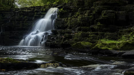 Time-lapse-of-spring-forest-cascade-waterfall-surrounded-by-trees-with-rocks-in-the-foreground-in-rural-landscape-of-Ireland