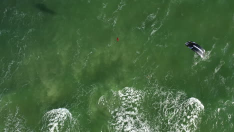 AERIAL:-Top-View-Rotating-Shot-of-Young-People-Kite-Surfing-Ride-on-Big-Green-Waves-in-the-Baltic-Sea