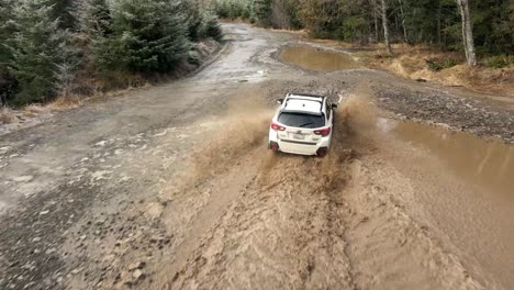 Chasing-a-Subaru-Crosstrek-through-deep-brown-mud-puddles,-aerial,-illustrative-editorial