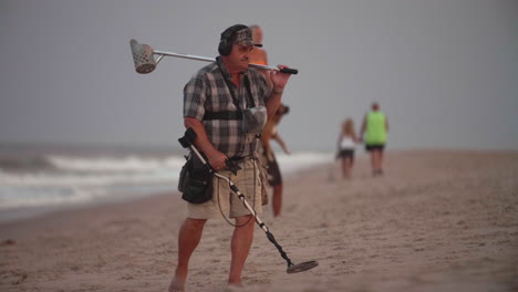 Man-looking-into-camera-with-metal-detector-on-beach