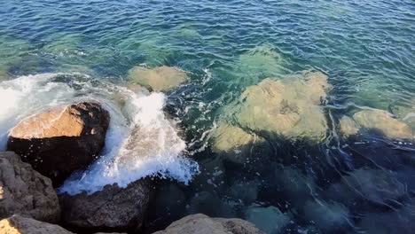 Pristine-clear-sea-water-crashing-against-rocky-shore-during-sunny-day