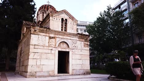 Church-of-Virgin-Mary-Gorgoepekoos-and-Saint-Eleutherius-while-woman-walking-away-in-downtown-of-Athens,-Greece