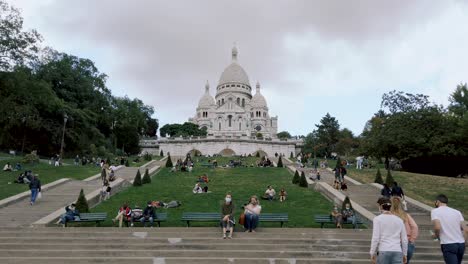 Statische-Aufnahme-Der-Treppe-Der-Basilika-Sacre-Coeur-Mit-Touristen,-Die-Während-Der-Coronavirus-Pandemie-In-Paris,-Frankreich,-Auf-Dem-Gras-Und-Der-Bank-Sitzen