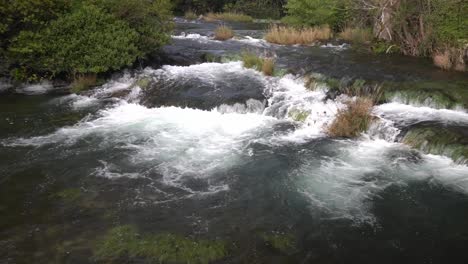 Wasser-Fließt-Von-Einer-Ebene-Zur-Anderen-Mit-Grünen-Und-Hellbraunen-Pflanzen,-Die-Im-Krka-Nationalpark-In-Kroatien-Mit-¼-Geschwindigkeit-Durchsetzt-Sind