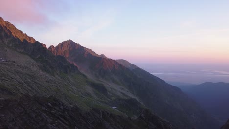 Atemberaubender-Panoramablick-Aus-Der-Luft-Auf-Die-Zerklüfteten-Berggipfel-Rumäniens-Und-Raues-Gelände-Mit-Farbenfrohem-Licht-Des-Sonnenuntergangs-In-Der-Landschaft-Und-Fernen-Wolken