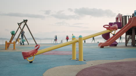 Colorful-Seesaw-Playground-is-Empty-in-Coronavirus-Quarantine-Times-while-a-Child-Swinging-in-the-Background-in-slowmo