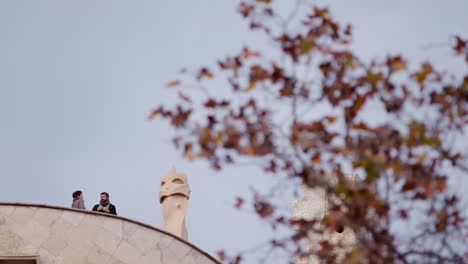 Two-people-talking-expressively-on-La-Pedrera-rooftop,-cloudy-winter-day
