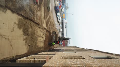 Vertical-time-lapse-with-construction-workers-operating-heavy-machinery-in-preparing-a-provisional-sidewalk-in-front-of-newly-build-houses-on-a-drowsy-overcast-day