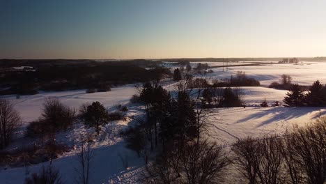 Beautiful-aerial-view-of-snow-covered-fields-and-forest-near-frozen-Sventaja-river-in-sunny-winter-day,-golden-hour,-wide-angle-drone-shot-moving-forward