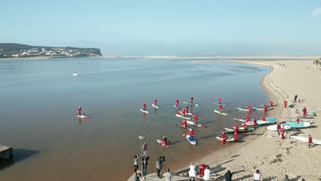People-In-Santa-Claus-Costume-Holding-Their-Paddle-Boards-Bound-To-The-Waters-Of-Obidos-Lagoon,-Portugal