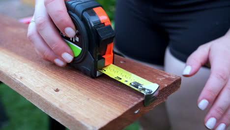 Slow-Motion-of-Woman's-Hands-Rolling-out-Measuring-Tape-on-Wood,-Woodworking-Outdoors-in-Daytime