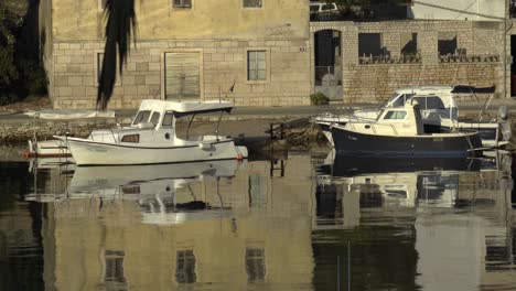 A-couple-of-boats-docked-along-a-road-in-Vela-Luka-in-Croatia-with-clear-reflection-in-the-water