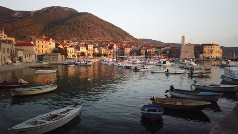Panning-view-of-Komiza,-its-many-docked-boats-in-the-cove,-and-the-castle-at-dusk-with-gentle-waves