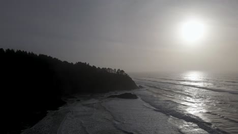 Golden-hazy-sunlight-reflects-off-rhythmic-ocean-waves-and-rugged-Washington-coastline,-aerial
