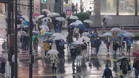 Personas-Con-Máscara-Durante-La-Pandemia-Con-Paraguas-Cruzando-La-Calle-En-Shinjuku-En-Una-Noche-Lluviosa-En-Tokio,-Japón