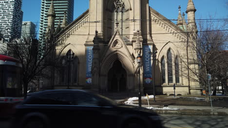 Wide-angle-on-a-streetcar-and-car-passing-through-frame,-with-a-slow-tilt-up-to-the-Cathedral-Church-of-Saint-James-tower