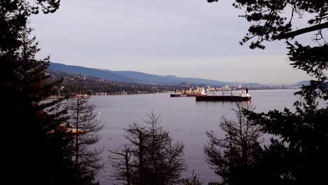 Cargo-ships-arrive-at-lit-up-Vancouver-port-in-evening,-long-shot