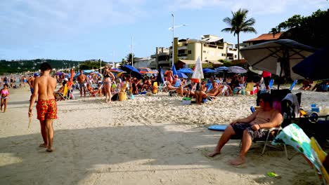 Dolly-in-of-people-resting-under-umbrellas-while-kids-play-in-the-sand-in-Bombas-and-Bombinhas-beaches,-Brazil
