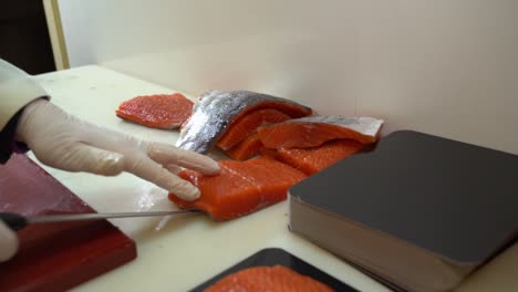 salmon-industry-worker-in-white-coat-moving-salmon-filet-from-chopboard-to-cutting-table---slow-motion