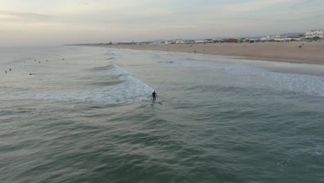 Surfer-Warten-Draußen-Im-Wasser-Auf-Ihre-Wellen,-Während-Ein-Surfer-Während-Der-Goldenen-Stunde-Eine-Welle-Springt