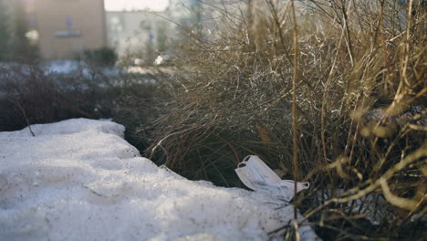 Slow-pan-of-white-face-mask-on-snowy-ground-by-bush,-car-passes