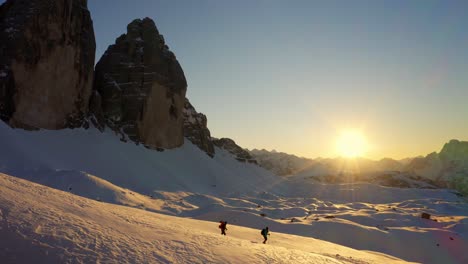 Two-hikers-exploring-Dolomite-and-walking-on-snow-at-sunset,-Tre-cime-di-Lavaredo