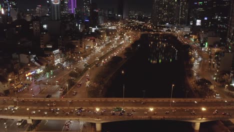 aerial-view-flying-across-busy-traffic-bridge,-main-road-and-river-at-night