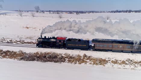 Luftaufnahme-Einer-Antiken-Dampflokomotive,-Die-Sich-Nähert,-Um-Personenwagen-Zu-Ziehen-Und-Rauch-Und-Dampf-Nach-Einem-Schneesturm-Zu-Blasen