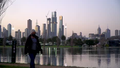 A-woman-wearing-a-mask-walks-by-a-city-skyline-during-the-global-coronavirus-pandemic