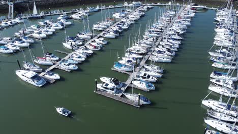 Sailboats-and-yachts-moored-along-Conwy-marina-luxury-waterfront-aerial-view-tracking-small-boat