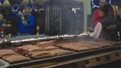 People-cooking-sausages-on-a-grill-at-a-Christmas-market-in-Hamburg,-Germany,-in-Dec-2019,-with-crowds-eating-in-the-background
