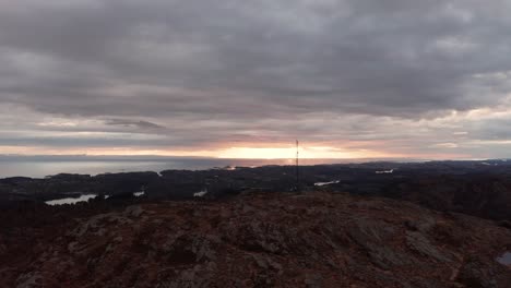 Tele-communication-mast-at-Norwegian-mountain-peak-in-front-of-cloudy-sunset-at-dawn---Late-night-ascending-aerial