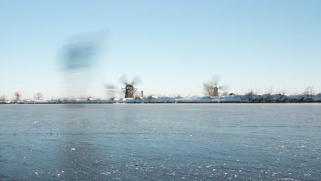 Time-lapse-of-ice-skaters-on-frozen-canal,-Netherlands-windmill-winter-scenery