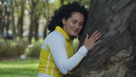 Jib-up-of-a-young-activist-woman-smiling-while-hugging-and-stroking-a-tree-with-love-in-a-park
