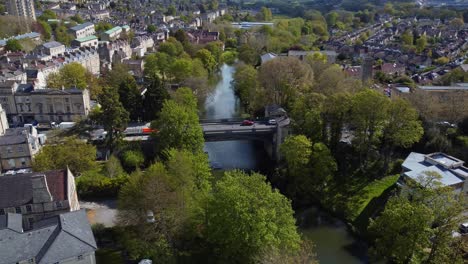 Vista-aerial-of-an-old-victorian-bridge-surrounded-by-a-luscious-green-and-inner-city-landscape,-Bath,-UK