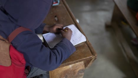 Niño-Africano-Pobre-Negro-Haciendo-La-Tarea,-Escribiendo-En-Su-Cuaderno-En-La-Escuela