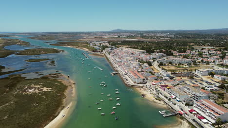 Barcos-Flotando-En-Un-Río-Tranquilo-Con-Edificios-Frente-Al-Mar-En-Cabañas-De-Tavira,-Portugal