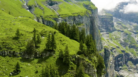 Flying-over-beautiful,-green-mountains-in-Switzerland-with-a-small-house-located-on-slope