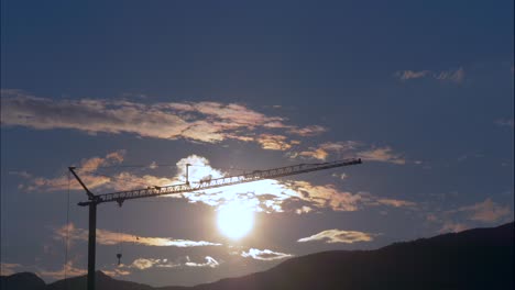 Time-lapse-shot-of-flying-clouds-against-blue-sky-and-silhouette-of-crane-in-sunset