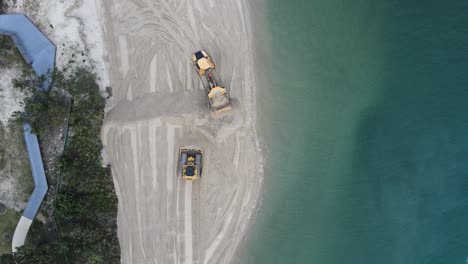 Hohe-Drohnenansicht-Großer-Maschinen,-Die-An-Einem-Küstenerneuerungsprojekt-Arbeiten-Und-Sand-In-Der-Nähe-Des-Meereswassers-Auffüllen