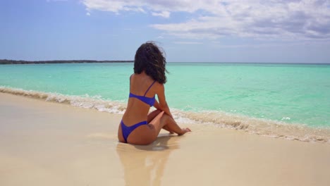 Young-Latin-American-Woman-Sat-on-Deserted-Beach-as-Turquoise-Waves-Gently-Roll,-Slow-Motion