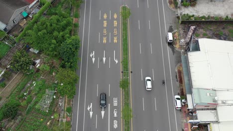 Bird-Eye-View-Aerial-Drone-Footage-of-Asphalt-Road-in-Taiwan,-drone-flying-along-the-straight-road,-tilting-upward-leading-to-residential-buildings-and-sky-and-mountains