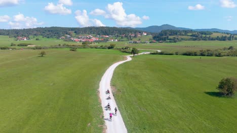 Aerial-Over-Group-Of-Tourists-Cycling-Along-Empty-Road-In-Countryside