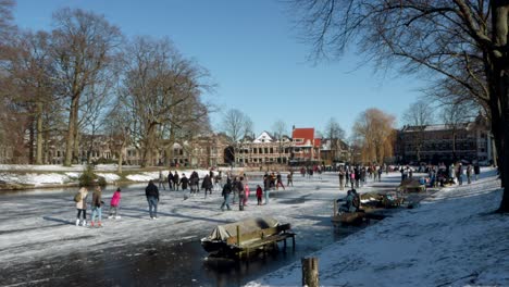 People-ice-skating-on-a-frozen-canal-in-Leiden,-the-Netherlands-on-a-sunny-winter-day-during-the-pandemic