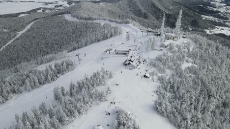 Zlatibor,-Tornik-top-of-the-mountain-with-gondola-and-ski-lift,-ski-slopes-and-antenna-with-hills-and-forest-covered-in-snow