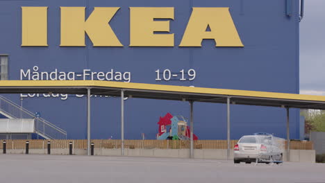 A-car-drives-past-an-abandoned-trolley-in-an-empty-IKEA-car-park