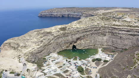 Ciudad-Portuaria-De-La-Cueva-De-Dwerja-Escondida-Detrás-De-La-Pared-Del-Acantilado-Rocoso,-Malta,-Antena