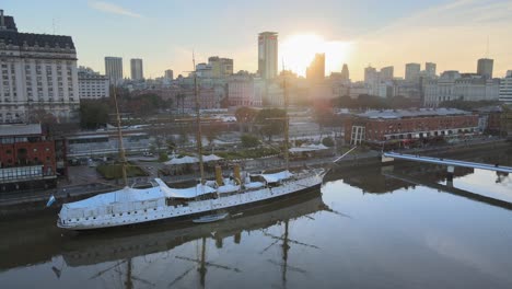 Forward-aerial-of-old-sailing-ship-and-Buenos-Aires-skyline-at-sunset