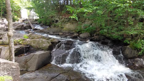 A-small-cascade-with-people-in-the-background-in-Ontario,-Canada,-wide-to-medium-lowering-shot-pan-right